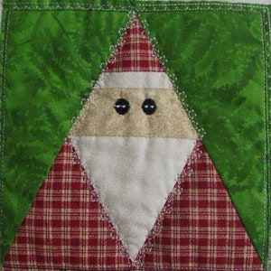 May include: A patchwork quilt block featuring a Santa Claus design. The block is made of red and white plaid fabric, beige fabric with a floral pattern, and white fabric. The Santa Claus has black eyes and a white beard.