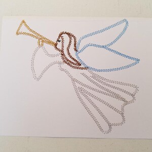 May include: A white card with a brown, blue, and yellow angel stitched on it. The angel is playing a trumpet.