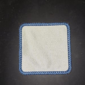 May include: A white square patch with a blue stitched border.