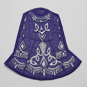 May include: Purple embroidered patch with a silver design. The design features a series of geometric shapes and patterns.