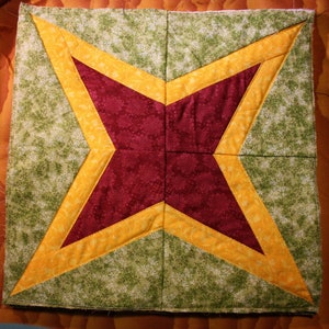 Puede incluir: Una colcha con un diseño de estrella en tonos de verde, amarillo y rojo. La estrella está hecha de varios cuadrados de tela cosidos juntos.