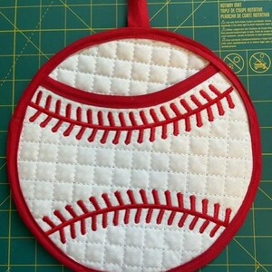 May include: White quilted pot holder shaped like a baseball with red stitching and a red loop for hanging.