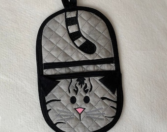 May include: A gray quilted oven mitt with a black cat design. The cat's tail is hanging down and its face is visible with black eyes and a pink nose.
