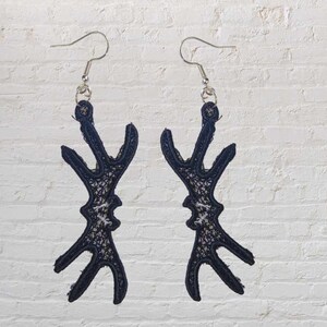 May include: A pair of black dangle earrings with a geometric design. The earrings are made of a delicate, lace-like material.