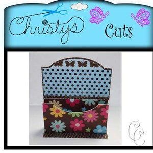 May include: A decorative paper craft organizer with a floral and polka dot pattern. The organizer has a brown base with colorful flowers and a blue polka dot interior. The top edge features butterfly cutouts and the text "Christy's Cuts".