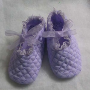 May include: A pair of lavender baby shoes with white lace trim and a quilted design. The shoes have satin ribbon ties.