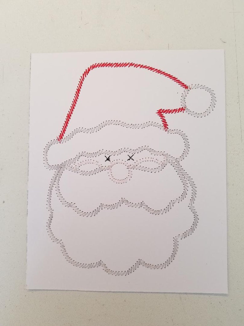 May include: A white paper craft with a red stitched outline of Santa Claus's face, hat, and beard. The eyes are marked with black Xs.