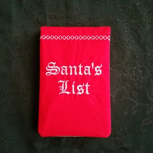 Peut inclure: Pochette en tissu rouge avec des coutures blanches et les mots "Santa's List" brodés en blanc.