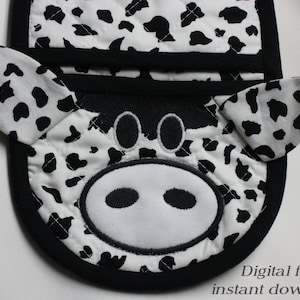 Op de afbeelding: Zwart-witte ovenwant met koeienprint, een zwarte rand en een schattig koeiengezicht met zwarte ogen en neusgaten.