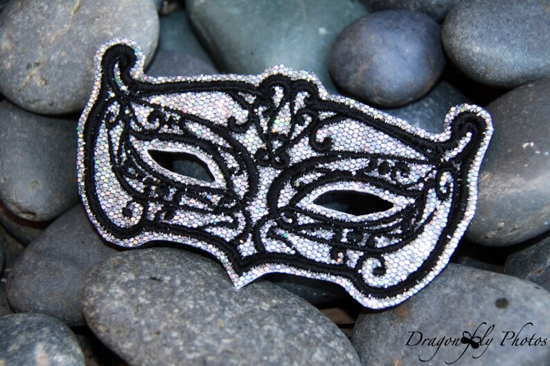 May include: A silver and black masquerade mask with intricate details and a sparkly finish.