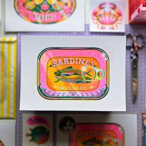 May include: A pink and green illustration of a can of sardines in olive oil. The can has a retro design with a wave pattern and the words "Sardines in Olive Oil" printed on it.
