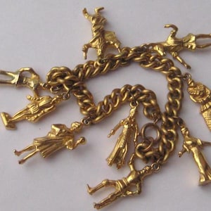 May include: A gold-tone metal charm bracelet featuring a thick curb chain link design. The bracelet is adorned with seven distinct gold-coloured charms, each depicting a different human figure in various poses, attached to the chain with small jump rings.