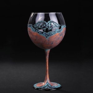 May include: A copper-colored wine glass with a blue and black decorative design around the rim. The glass has a wide bowl and a long stem.