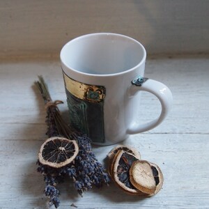 Puede incluir: Taza de cer&aacute;mica blanca con un dise&ntilde;o azul y dorado. La taza est&aacute; sobre una superficie de madera blanca con lavanda seca y rodajas de naranja.