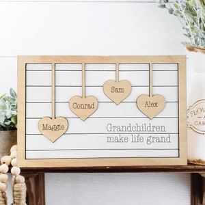 May include: Wooden sign with the text "Grandchildren make life grand" and four hanging wooden hearts with the names Maggie, Conrad, Sam, and Alex.