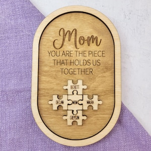 Könnte beinhalten: Holzplakette mit dem Text "Mama Du bist das Stück, das uns zusammenhält" und einem Puzzle-Design mit den Namen Beckett, Declan, Mama, Maura und Greyson.