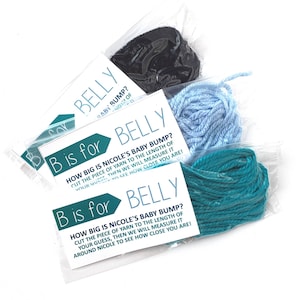 May include: Two cards with the text "B is for BELLY" and instructions for a baby bump guessing game. The cards are packaged with three different colors of yarn: black, light blue, and teal.