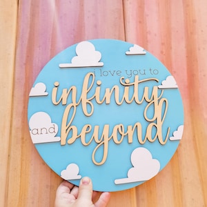 May include: A round, light blue wooden sign with the phrase "i love you to infinity and beyond" in cursive and block letters. White cloud cutouts are placed around the edge of the sign.