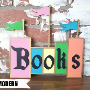May include: A colorful wooden bookend with the word "Books" in black gothic font. The bookend features pink, blue, yellow, green, and orange blocks, with small flags on top. The word "MODERN" is printed at the bottom.