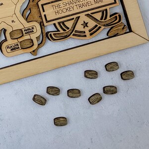 May include: A close-up of nine wooden hockey pucks on a white surface. The pucks are brown and have a wood grain texture. The pucks are arranged in a random pattern.
