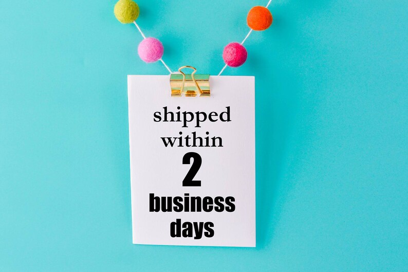 May include: A white card with a gold paper clip hanging from a string of colorful pom-poms against a blue background. The card says "shipped within 2 business days".