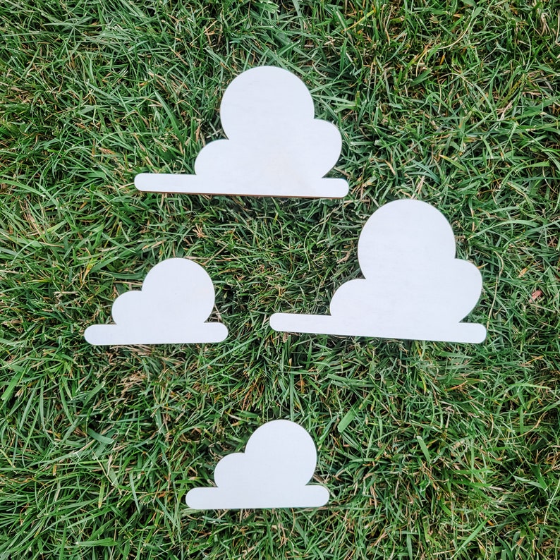 May include: Four white wooden clouds of various sizes, arranged on a green grassy surface.