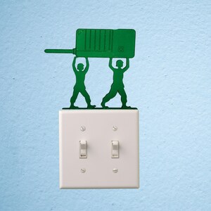 Puede incluir: Silueta verde de dos soldados de juguete sosteniendo un walkie-talkie verde sobre un interruptor de luz blanco. El interruptor tiene dos interruptores y est&aacute; montado en una pared azul claro.