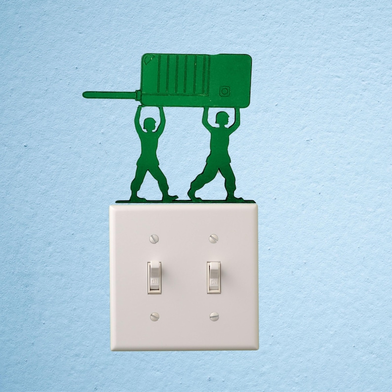 Puede incluir: Silueta verde de dos soldados de juguete sosteniendo un walkie-talkie verde sobre un interruptor de luz blanco. El interruptor tiene dos interruptores y est&aacute; montado en una pared azul claro.