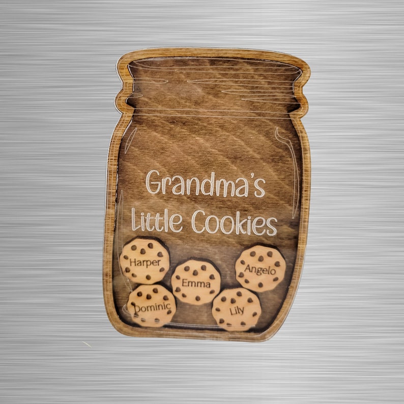 May include: Wooden jar-shaped sign with the text "Grandma's Little Cookies." Inside the jar are five wooden cookies, each with a name: Harper, Emma, Angelo, Dominic, and Lily. The sign is made of stained wood.