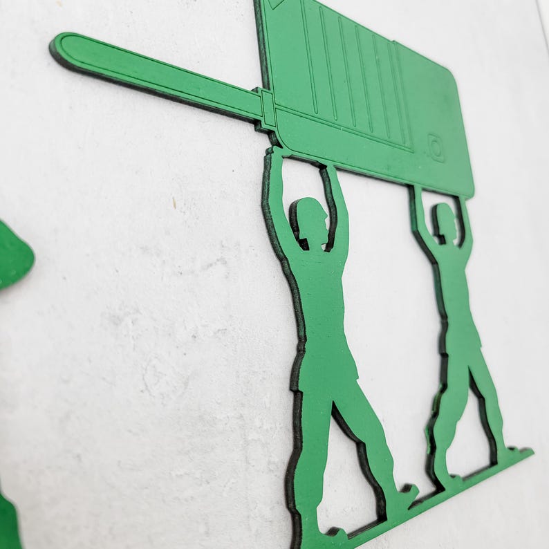 Puede incluir: Arte de pared de madera verde que representa dos siluetas de soldados de juguete levantando un gran rect&aacute;ngulo verde. Los soldados est&aacute;n en una pose cl&aacute;sica, sosteniendo la pieza rectangular sobre sus cabezas. El arte est&aacute; montado en una pared blanca.
