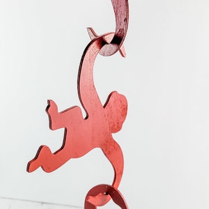 Puede incluir: Un m&oacute;vil de madera rojo con tres monos colgados unos de otros. Los monos est&aacute;n en una pose juguetona con los brazos y las piernas extendidos.