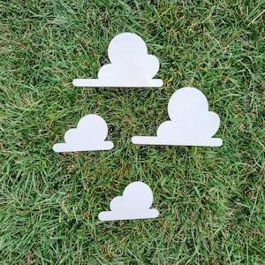 May include: Four white wooden cloud shapes on a green grassy background. The clouds are different sizes and shapes.