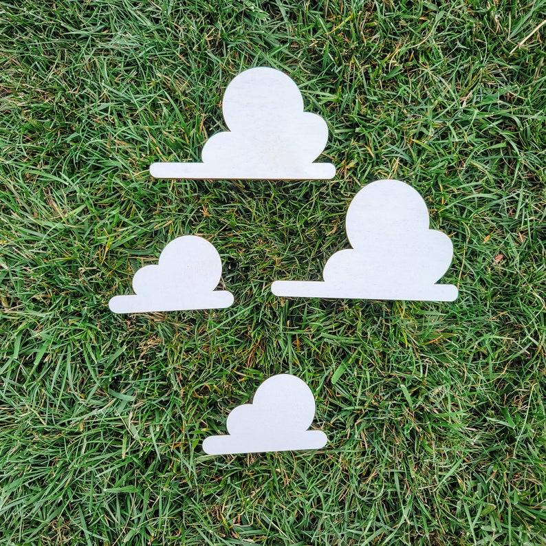 May include: Four white wooden cloud shapes on a green grassy background. The clouds are different sizes and shapes.
