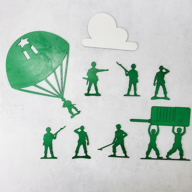 Puede incluir: Un conjunto de soldados de juguete de madera verde en varias poses, incluyendo un soldado con paraca&iacute;das y una nube blanca recortada. Los soldados est&aacute;n dispuestos sobre una superficie blanca.