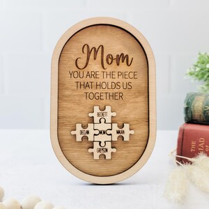 Könnte beinhalten: Holzplakette mit dem Text "Mama Du bist das Stück, das uns zusammenhält" und einem Puzzle-Motiv mit den Namen Beckett, Declan, Mama, Maura und Greyson.