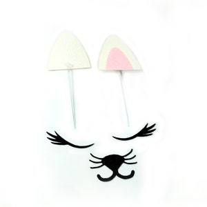 May include: A set of white felt cat ears with pink inside, black felt eyelashes, and a black felt cat nose. The ears are on white sticks.