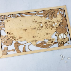 May include: A wooden map of the United States with baseballs marking locations. The map is framed in wood and includes the text "The Shannon Family Baseball Travel Map".