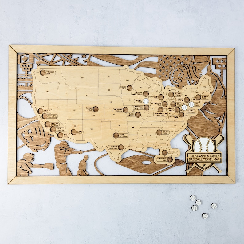 May include: A wooden map of the United States with baseball stadiums marked. The map is framed in wood and has a baseball theme with a baseball bat and ball in the bottom right corner. The text "The Shannon Family Baseball Travel Map" is printed below the baseball bat and ball.