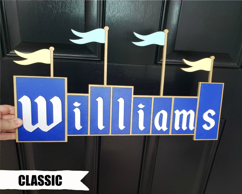 May include: A blue and gold wooden sign in the shape of a castle with the name "Williams" in white lettering. The sign has light blue and yellow flags on top, and the word "CLASSIC" is written at the bottom.