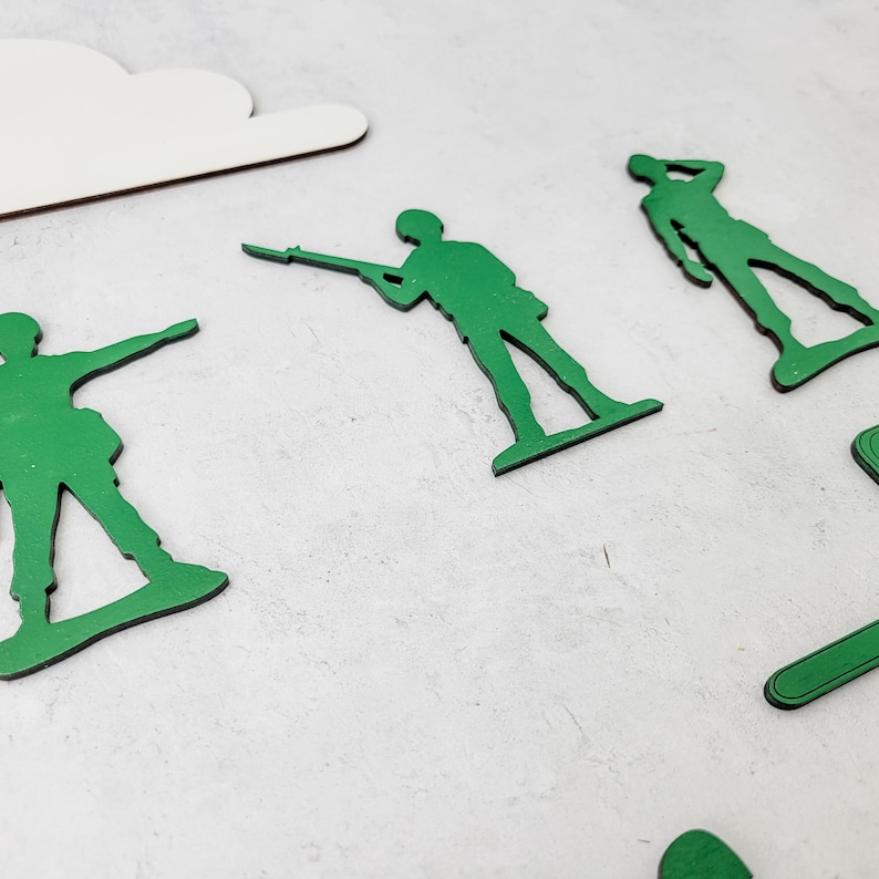 Puede incluir: Figuras de soldados de juguete verdes en varias poses dispersas sobre una superficie gris claro. Una nube blanca de madera recortada est&aacute; en la esquina superior izquierda. Los soldados de juguete est&aacute;n en diferentes posiciones, algunos sosteniendo rifles.