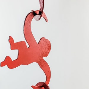 Puede incluir: Un m&oacute;vil de madera rojo con tres monos colgando de las colas el uno del otro. Los monos est&aacute;n todos mirando en la misma direcci&oacute;n y est&aacute;n en l&iacute;nea.