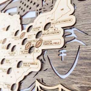 K&ouml;nnte beinhalten: Eine Holzkarte der Vereinigten Staaten mit Stadionnamen und Footballs. Die Karte besteht aus geschichtetem Holz mit hellbraunem Finish. Zu den Stadionnamen geh&ouml;ren Gillette Stadium, Metlife Stadium und Lincoln Financial Field.