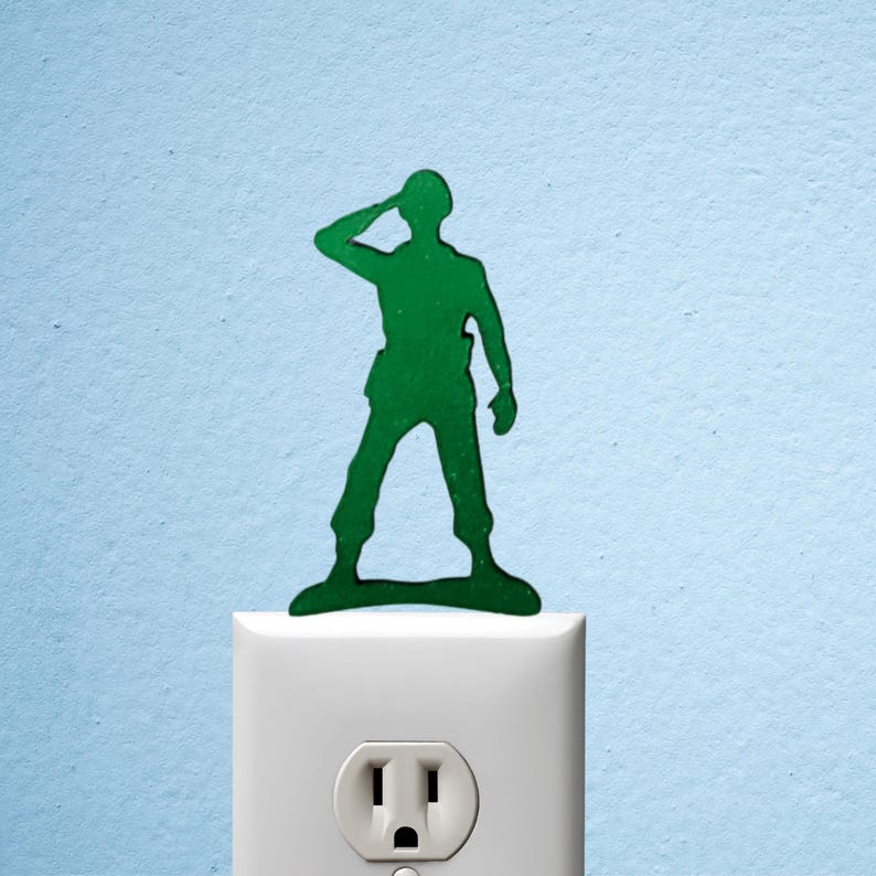 Puede incluir: Silueta verde de un soldado de juguete saludando, colocado sobre un enchufe blanco contra un fondo azul claro. El soldado de juguete es un dise&ntilde;o cl&aacute;sico, a menudo utilizado como elemento decorativo.