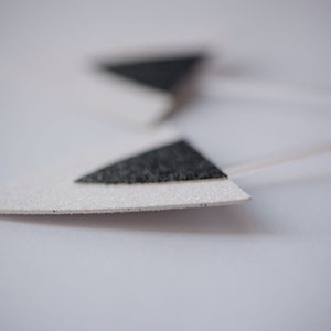 May include: Two white triangle-shaped paper earrings with black glitter accents.