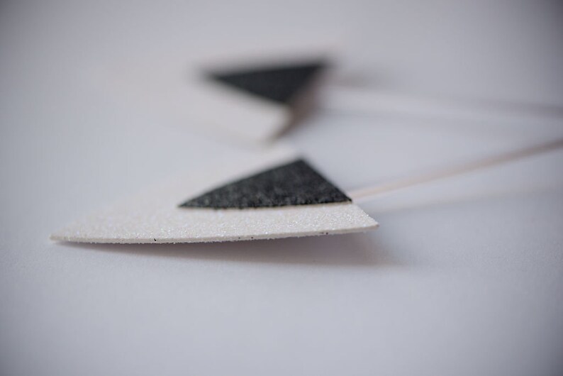 May include: Two white triangle-shaped paper earrings with black glitter accents.