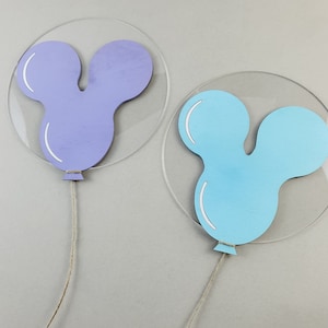 K&ouml;nnte beinhalten: Zwei ballonf&ouml;rmige Dekorationen mit einer Mickey-Maus-Silhouette. Der Ballon links ist lila und der Ballon rechts ist blau.