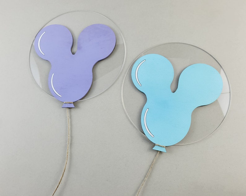 K&ouml;nnte beinhalten: Zwei ballonf&ouml;rmige Dekorationen mit einer Mickey-Maus-Silhouette. Der Ballon links ist lila und der Ballon rechts ist blau.