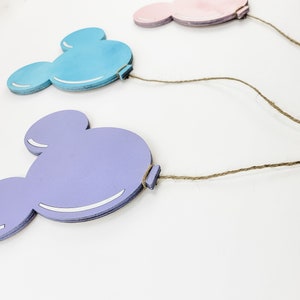 K&ouml;nnte beinhalten: Drei Mickey-Maus-f&ouml;rmige Holzballons in Rosa, Blau und Lila mit befestigtem Bindfaden.