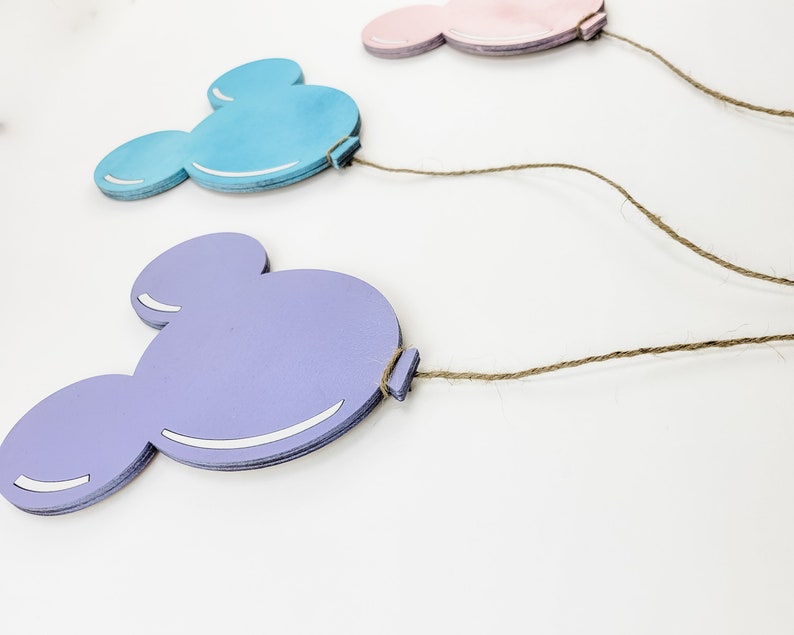 K&ouml;nnte beinhalten: Drei Mickey-Maus-f&ouml;rmige Holzballons in Rosa, Blau und Lila mit befestigtem Bindfaden.