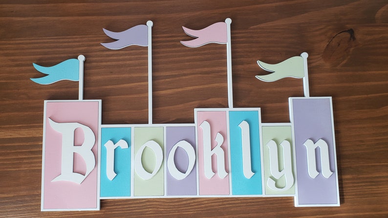 May include: A pink, blue, green, and purple castle-shaped name sign with the name "Brooklyn" spelled out in white letters.